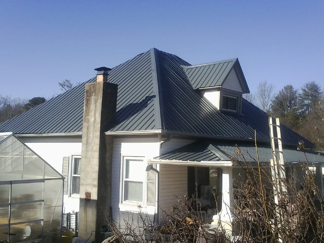 Dark blue standing seam metal roof on a white farmhouse with dormer — Slate & Tile Roof Repair by Roofing Brothers in Gwynn