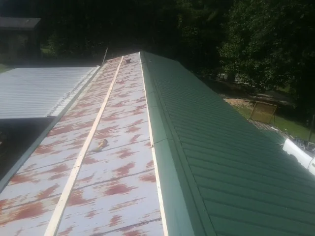 Old rusted panels beside newly installed green metal roofing — Wind Damage Roof Repair by Roofing Brothers in Gwynn