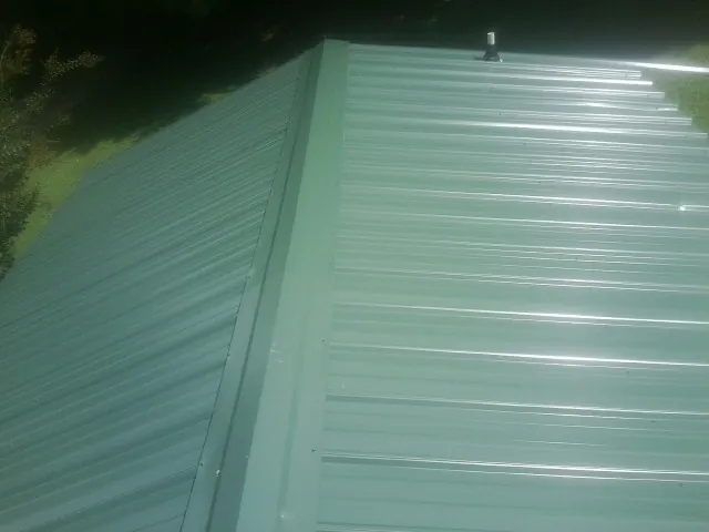 New green metal panels meeting at the ridge of a roof — Flat Roof Repair work by our crew in Gwynn