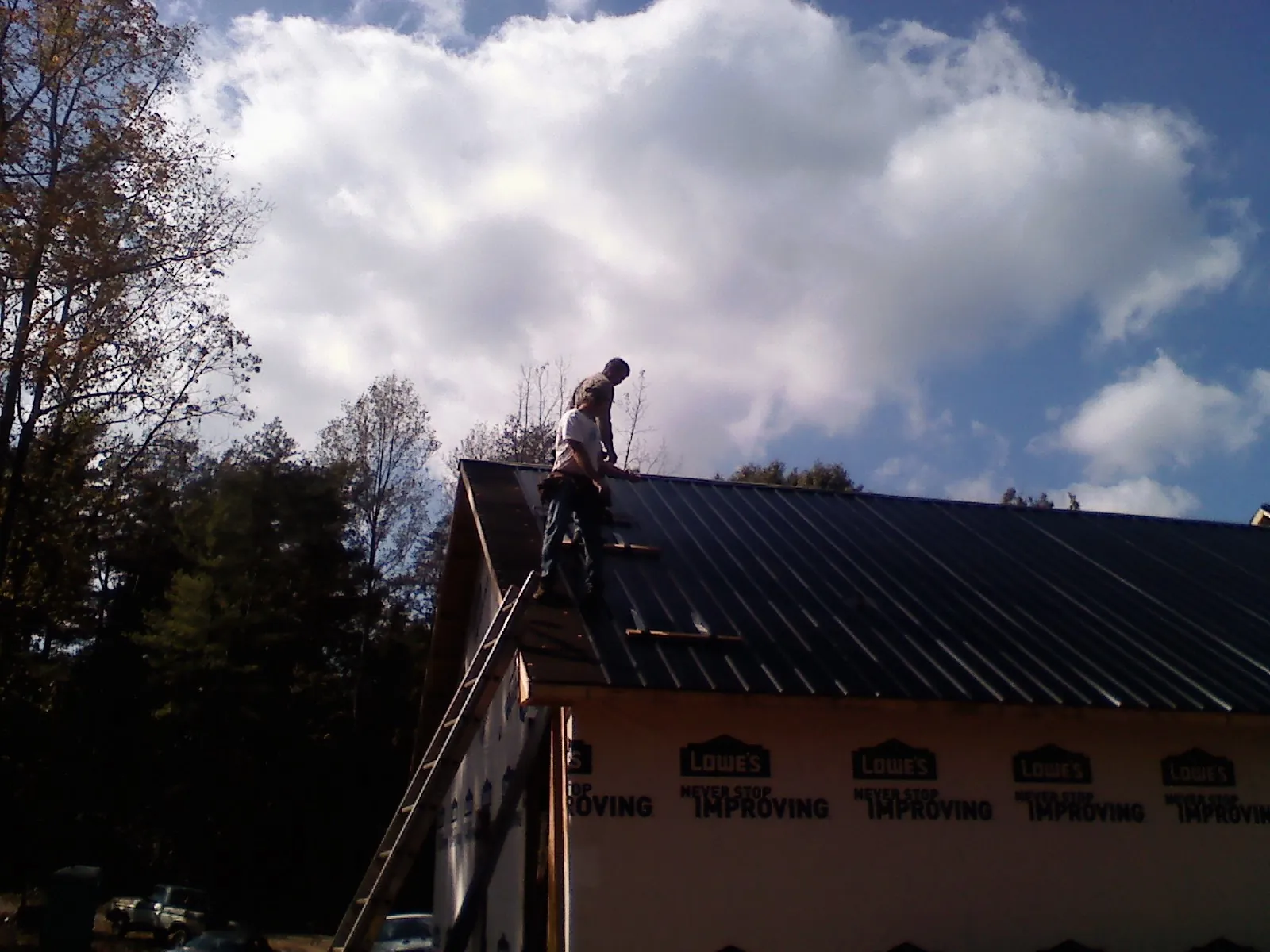 Roofer fastening dark metal panels high against a cloudy sky, from a Roof Inspection job in Gwynn