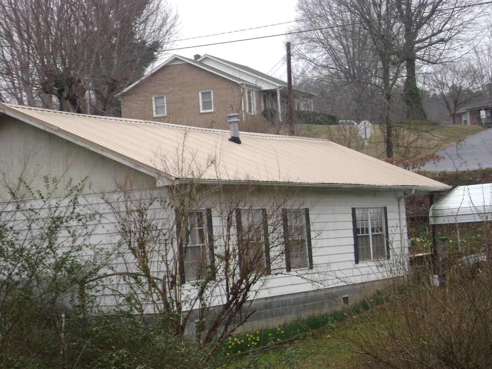 Tan metal roof on a white sided house set into a hillside — Commercial Roofing by Roofing Brothers in Gwynn