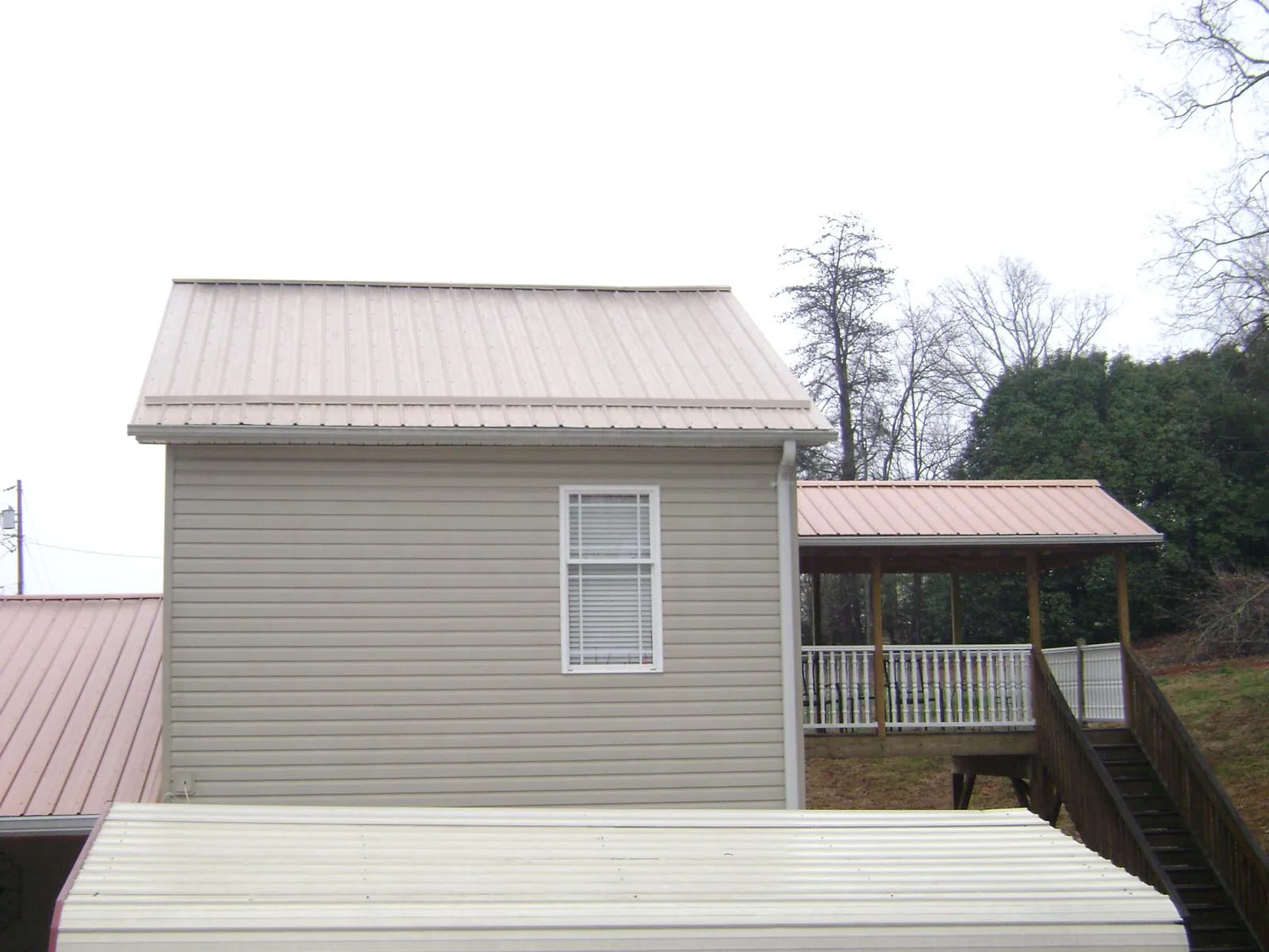 Tan metal roofs on a two story addition and attached porch, from a Roof Replacement job in Gwynn